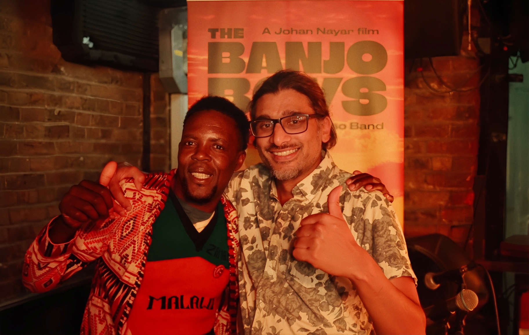 Yosefe with thumbs up in front of The Banjo Boys poster at The Madalitso Experience