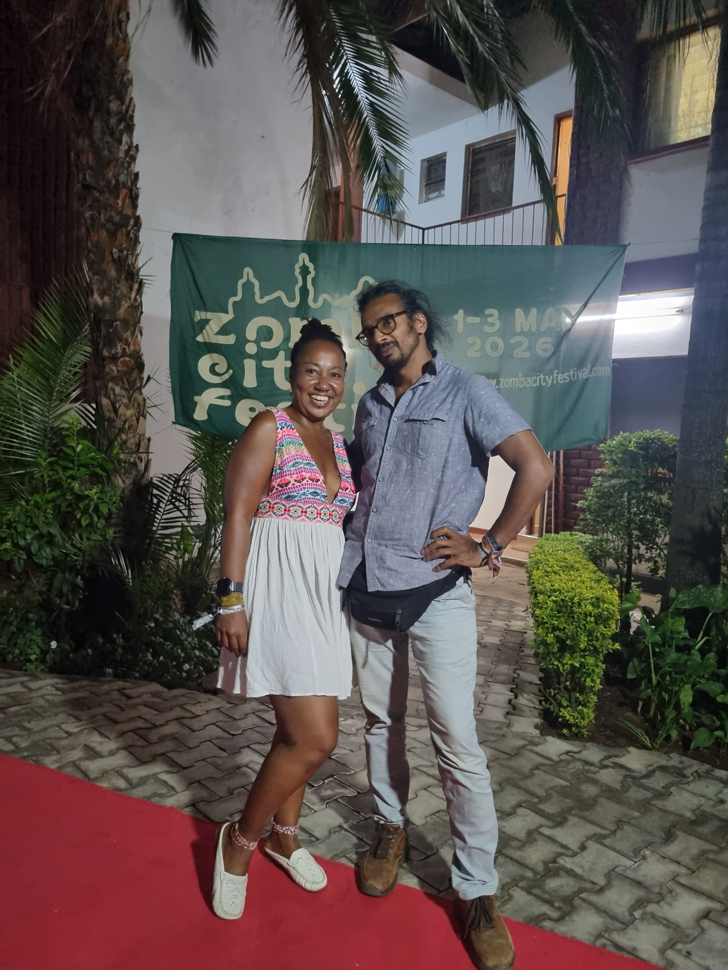Narrator-producer Neil Nayar on the red carpet with a guest in front of the Zomba City Festival banner
