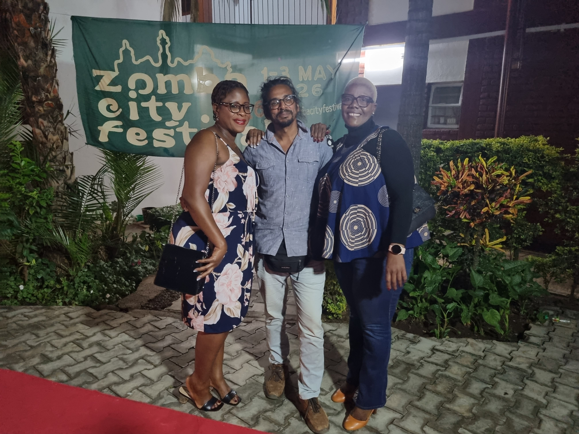 Neil Nayar with two guests on the red carpet in front of the Zomba City Festival banner
