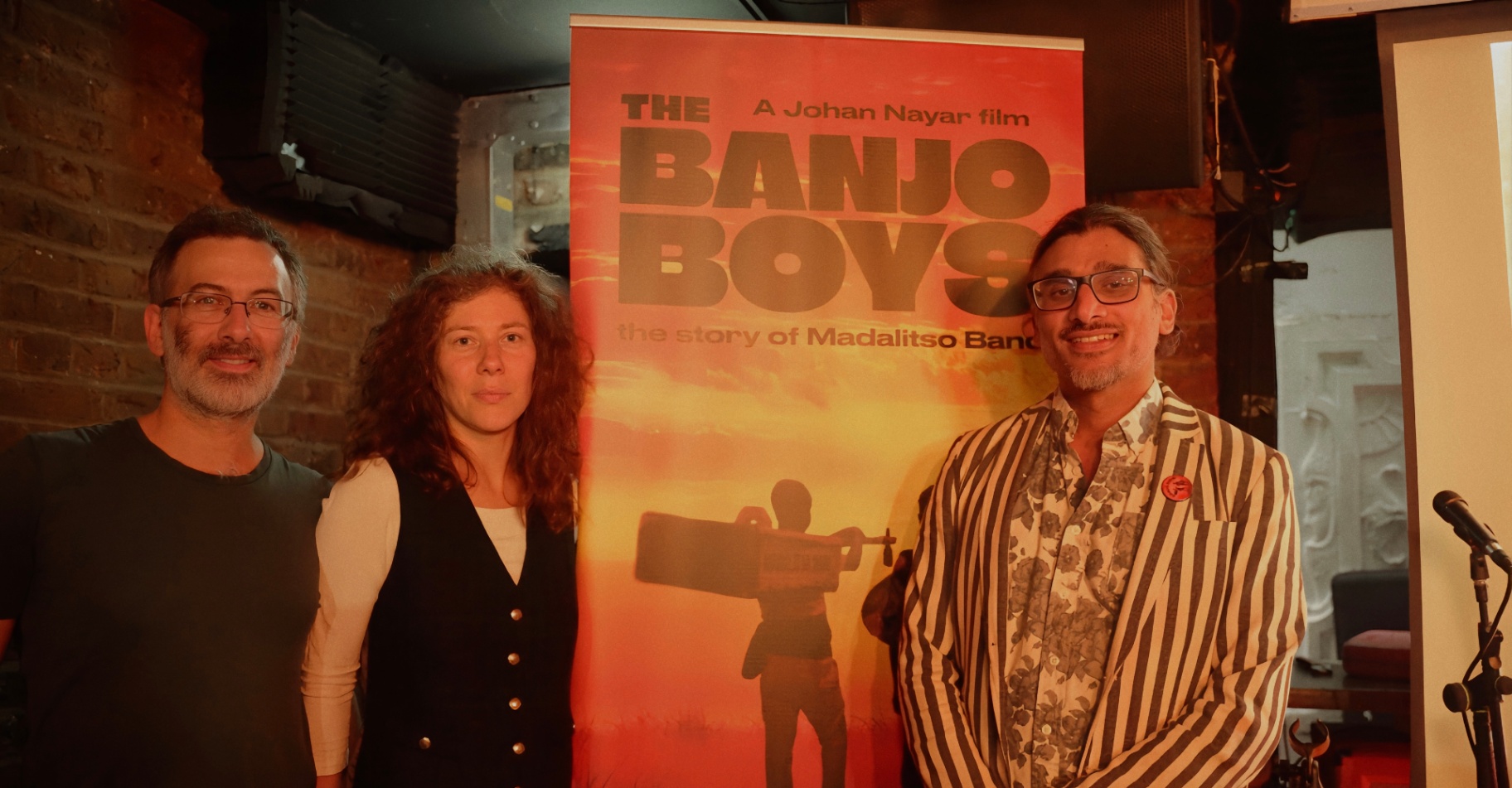 Guests beside the Banjo Boys poster at The Madalitso Experience with Johan Nayar at the Troubadour, London — Johan Nayar with old uni mate, George Ttoouli and Daniela
