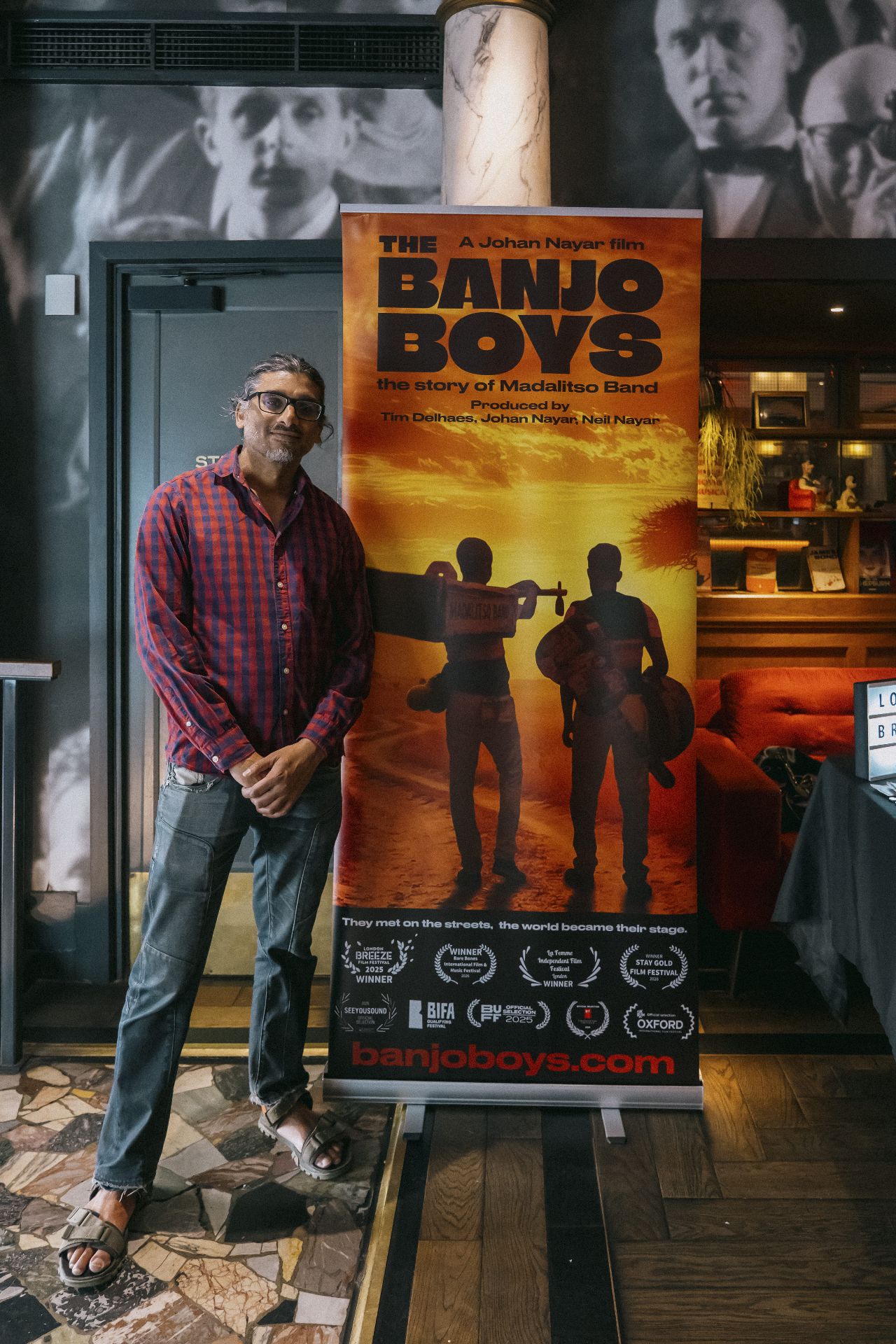 Director Johan Nayar posing beside The Banjo Boys banner in the Bristol cinema foyer